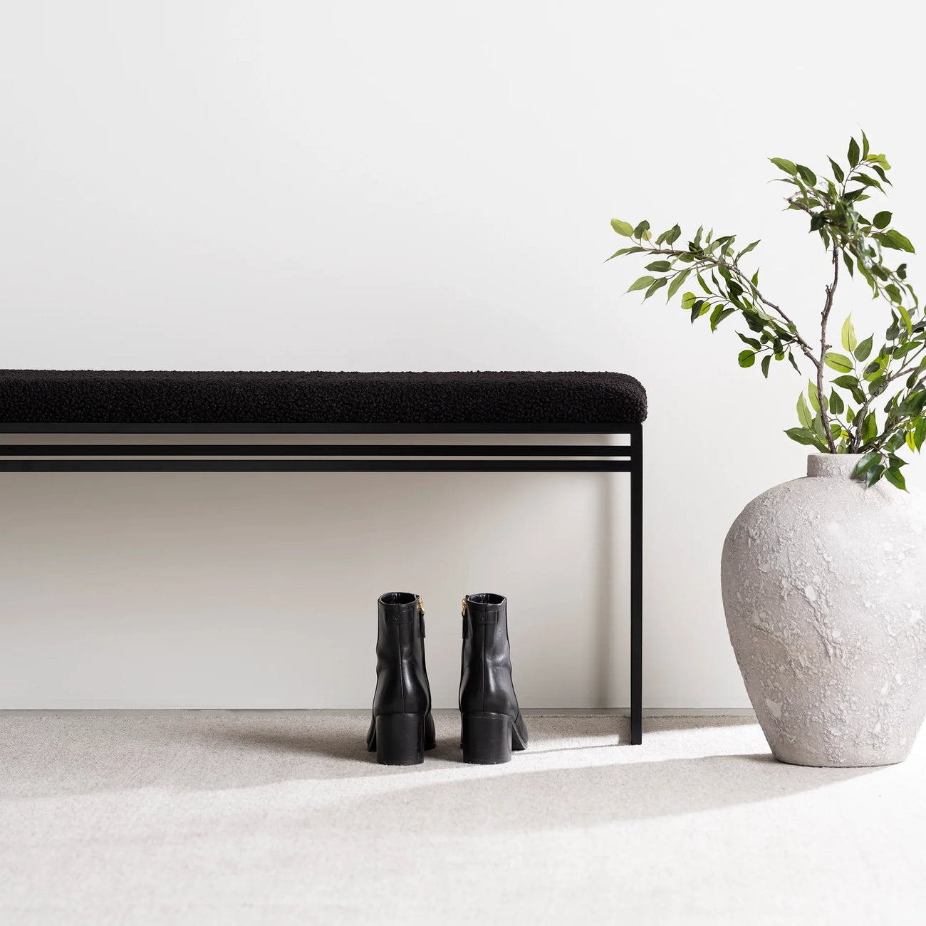 Wilma black bouclé bench with clean lines, minimalist design, and stylish black boots beside a textured vase.