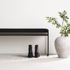 Wilma bench in black with vegan leather seat, minimalist design, with black boots and a plant beside it.