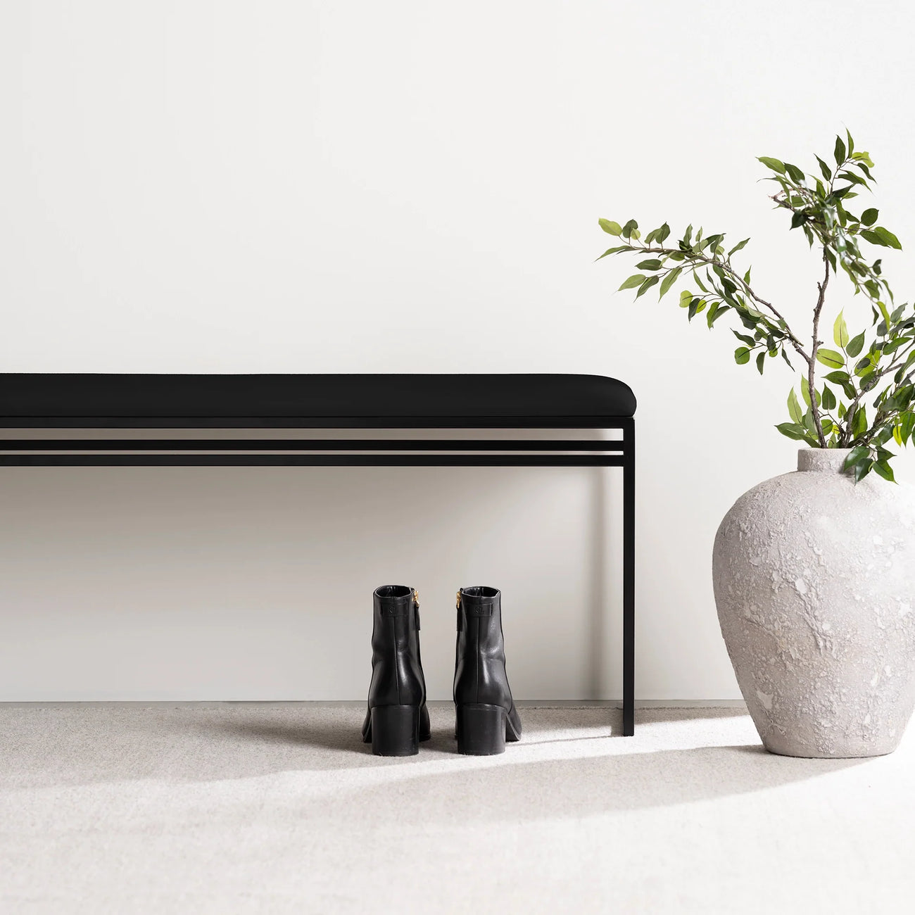 Wilma bench in black with vegan leather seat, minimalist design, with black boots and a plant beside it.