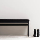 Oak Bench Alva with black oak frame and black bouclé cushion alongside stylish black boots