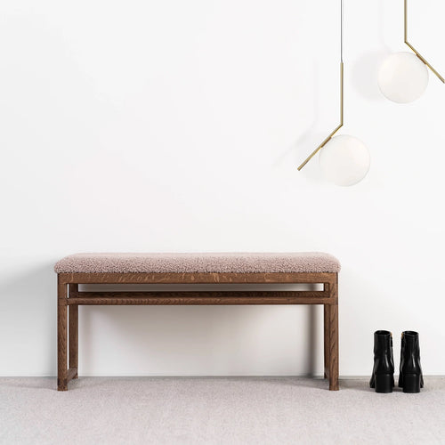 Wilma wood bench in dark oak with greige bouclé, ideal for modern interiors, styled with black boots and elegant lighting.