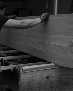 Craftsman handling a large slab of solid oak during the tabletop manufacturing process at the by Crea factory. Swedish handmade furniture in progress.